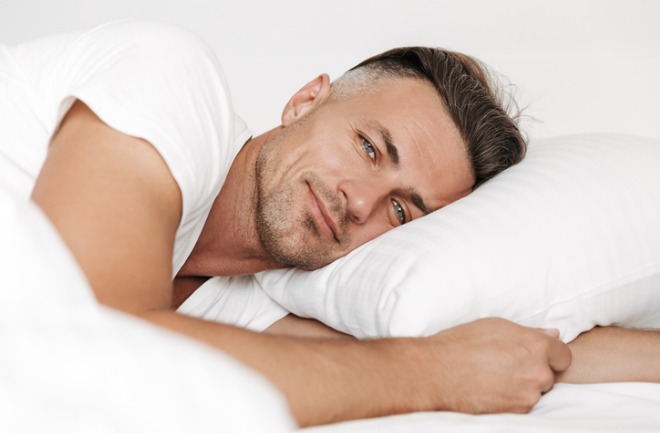 confira a tendência por trás de definir a mandíbula entre os homens homem posando para foto deitado em cama com lençóis brancos após definir a mandíbula