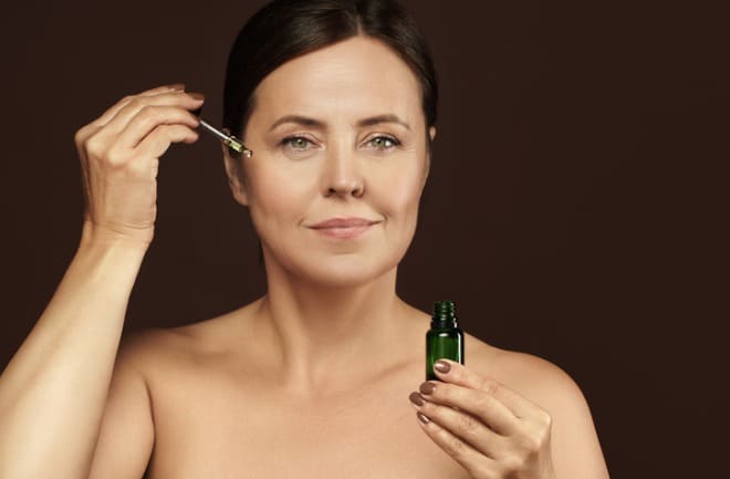 confira os melhores produtos de skin care após lifting cirúrgico Mulher aplicando sérum facial em sua rotina de skin care após lifting cirúrgico